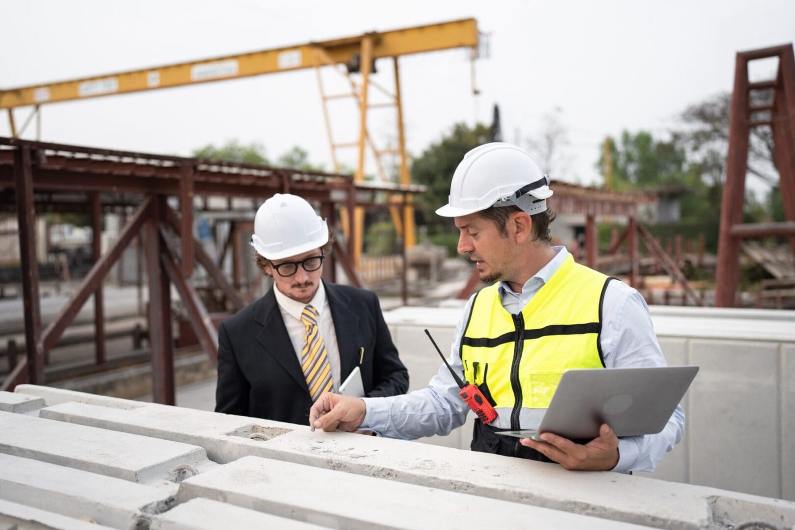 Two men in hard hats and vests working on a construction site.